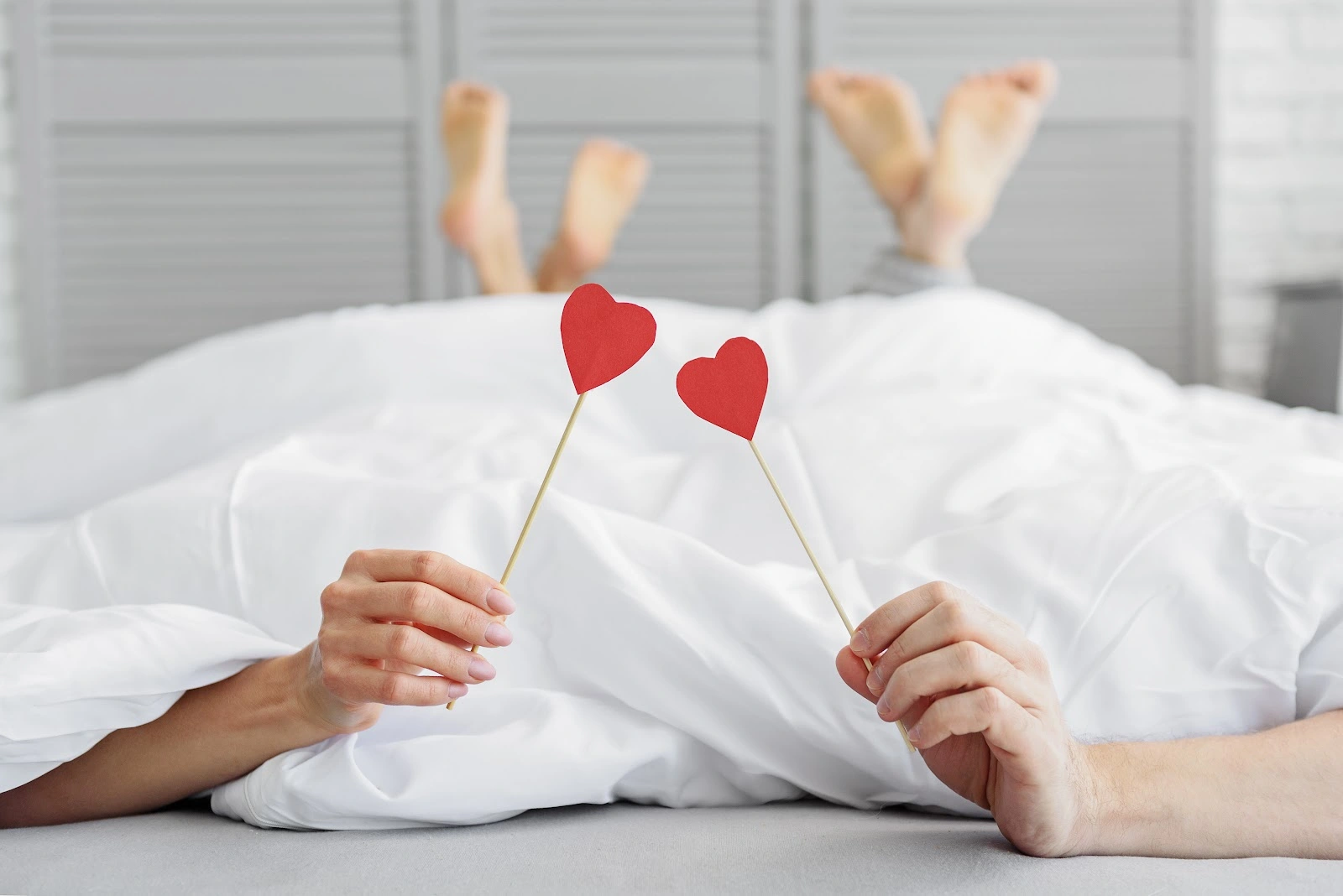 a couple holding paper red hearts glued to a stick in bed